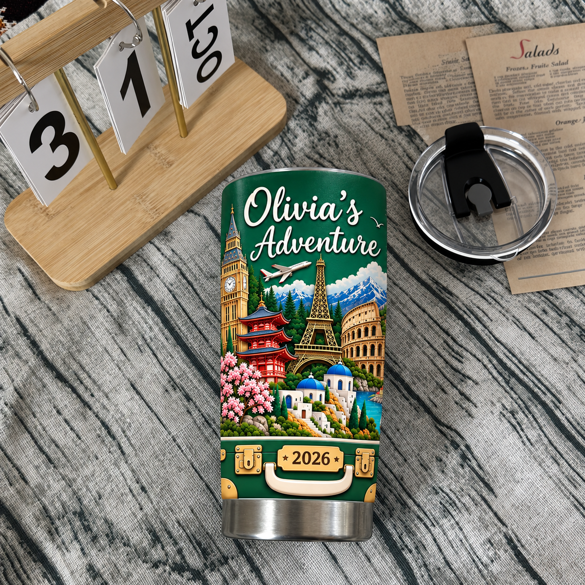 Trip memory keepsake tumbler resting on a textured surface alongside a calendar block and a clear lid.