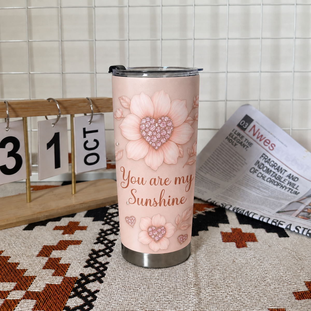 A pink floral tumbler stands next to a wooden desk calendar showing October 31 and an open newspaper.