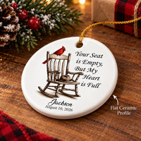 Flat ceramic memorial ornament angled on a wooden surface beside pine branches and a gift box.